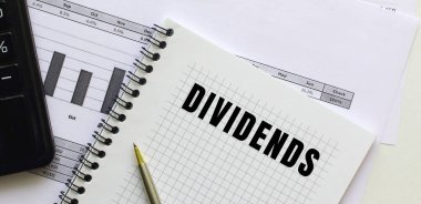 Finansal tabloların üzerinde duran bir not defterinin sayfasına DiviendDS 'i yaz. Hesap makinesinin yanında. İş konsepti.