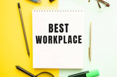 Ofis masasında ofis malzemeleriyle birlikte en iyi çalışma yeri yazılı defter. Sarı arkaplan kavramı. İş konsepti.