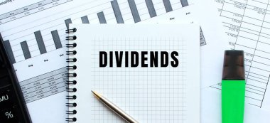 Finansal tabloların üzerinde duran bir not defterinin sayfasına DiviendDS 'i yaz. Hesap makinesinin yanında. İş konsepti.