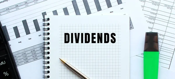 Finansal tabloların üzerinde duran bir not defterinin sayfasına DiviendDS 'i yaz. Hesap makinesinin yanında. İş konsepti.