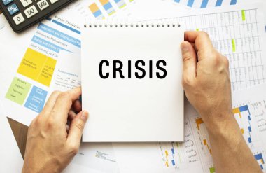 İş adamı not defterini CRISIS ile birlikte tutuyor. Masaüstünün mali tabloları. Mali ve iş konsepti.