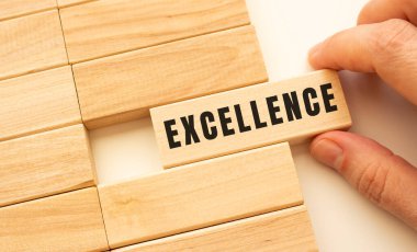 Elin üzerinde EXCELLENCE yazan tahta bir küp tutuyor. Pozitif düşünce konsepti