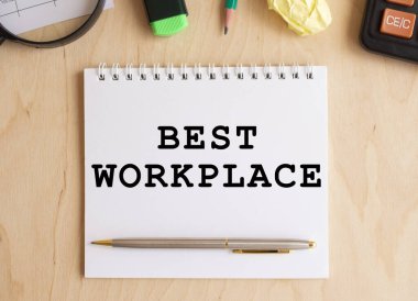 Hesap makinesi ve ofis malzemelerinin yanında, ahşap bir masanın üzerinde en iyi çalışma yeri yazılı not defteri. İş konsepti.