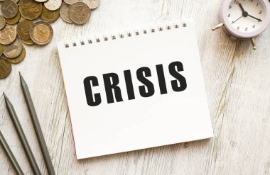 CRISIS bir not kağıdına mesaj atmış. Bozuk paralar dağınık, kalemler gri ahşap arka planda. Mali konsept.