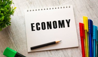 Bir yay üzerinde beyaz bir çarşaf üzerinde ECONOmy yazılı bir defter renkli kalemlerle ahşap bir masada yatıyor. İş konsepti.