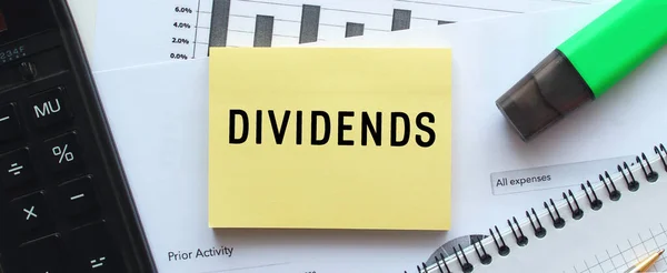 Finansal tabloların üzerinde duran bir not defterinin sayfasına DiviendDS 'i yaz. Hesap makinesinin yanında. İş konsepti.