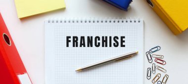 Beyaz bir arkaplanda, belge klasörünün ve ofis malzemelerinin yanında FRANCHISE yazılı not. İş konsepti.