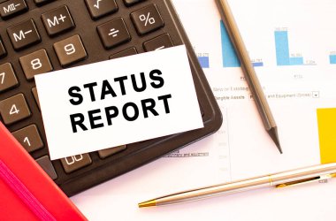 Metal kalemli, hesap makineli ve mali tablolu beyaz kart üzerinden STATUS metni. İş ve mali konsept