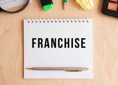 Hesap makinesi ve ofis malzemelerinin yanında, ahşap bir masanın üzerinde FRANCHISE yazılı not. İş konsepti.