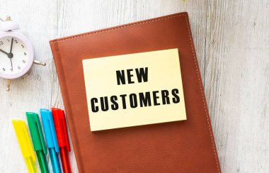 Bilgisayarın, hesap makinesinin ve ofis malzemelerinin yanında, beyaz arka planda NEW CUSTOMERS yazılı not defteri. İş konsepti.