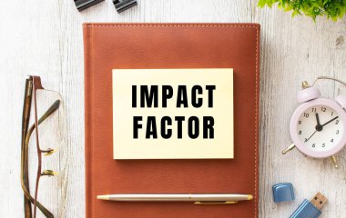 Tahta bir masanın üzerinde IMPACT FACTOR yazısıyla not et. Kahverengi günlük ve kalem. İş konsepti.