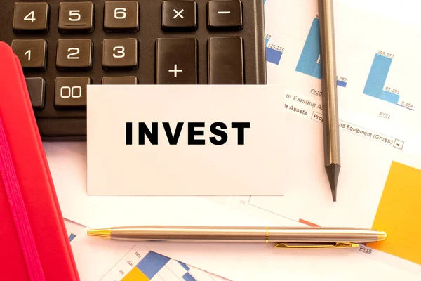 Text Invest Vitt Kort Med Metallpenna Miniräknare Och Finansiella Diagram — Stockfoto