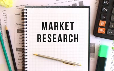 Ofis masasında, hesap makinesi ve ofis malzemelerinin yanında MARKET RESEARCH yazılı not defteri.