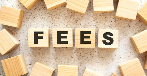 The word FEES consists of wooden cubes with letters, top view on a light background. Work space.