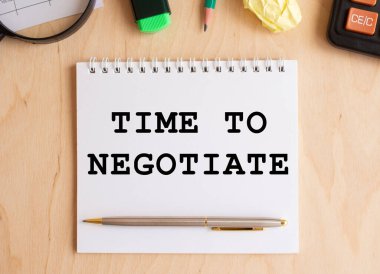 Hesap makinesi ve ofis malzemelerinin yanında, ahşap bir masada pazarlık yapmak için mesaj zamanı olan bir not. İş konsepti.