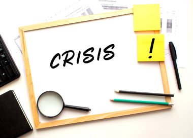 CRISIS metni beyaz bir ofis tahtasına yazılmış. Ofis malzemeleriyle birlikte çalışma masası. İş ve mali konsept.
