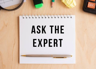 Notepad with text ASK THE EXPERT on a wooden table, near calculator and office supplies. Business concept.