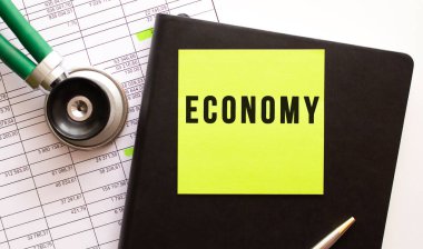 Üzerinde ECONOMY yazan siyah etiketli siyah defter. Yakınlarda bir fonendoskop var. Yakın plan..