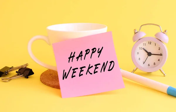 Pink paper with the text HAPPY WEEKEND on a white cup. Clock, pen on a yellow background. Design concept.