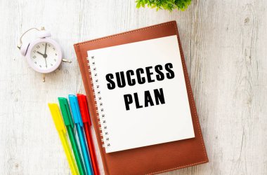 Tahta bir masanın üzerinde SUCCESS Planı yazan bir not. Kahverengi günlük ve kalemler. İş konsepti.