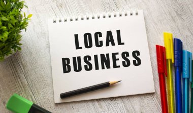 Üzerinde LOCAL BUSINESS yazan bir yay üzerindeki beyaz bir defter renkli kalemlerle ahşap bir masanın üzerinde yatar. İş konsepti.