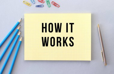 Kalemlerin, ataçların ve ataçların yanındaki gri arkaplanda, defterde nasıl çalıştığı. Kavram.