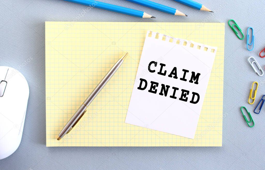 CLAIM DENIED is written on a piece of paper that lies on a notebook next to office supplies. Business concept.
