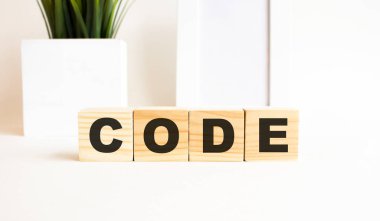 Beyaz bir masanın üzerinde harfler olan tahta küpler. Kelime kod. Fotoğraf çerçeveli beyaz arkaplan, ev bitkisi.