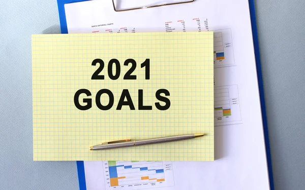 2021 GOALS text written on notepad with pencil. Notepad on a folder with diagrams. Financial concept.