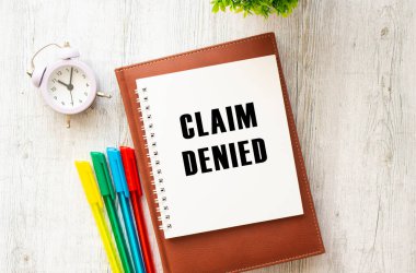 Üzerinde CLAIM DENIED yazan ahşap bir masa. Kahverengi günlük ve kalemler. İş konsepti.