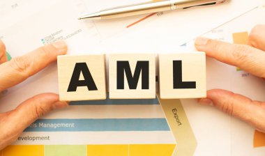 Çalışma masasının üzerinde AML harfleri olan tahta küpleri tutan eller. Üst görünüm