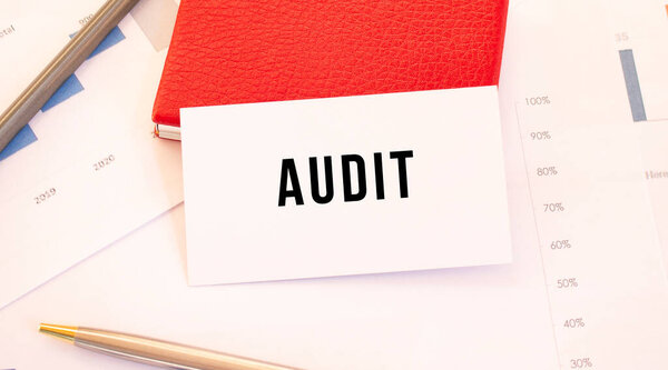 White business card with text AUDIT lies next to red business card holder.