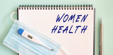 Defterde tıbbi koruyucu maske ve termometre var. KADINLAR SAĞLIK bir defter içinde mesaj. Tıbbi konsept.