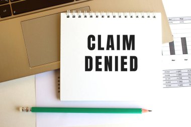 Laptop klavyesinde CLAIM DENIED yazan not defteri var. En az çalışma alanı.