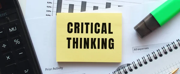 Text CRITICAL THINKING on the page of a notepad lying on financial charts on the office desk. Near the calculator. Business concept.