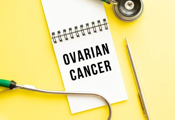 OVARIAN CANCER is written in a notebook on a color table next to pen and a stethoscope. Medical concept