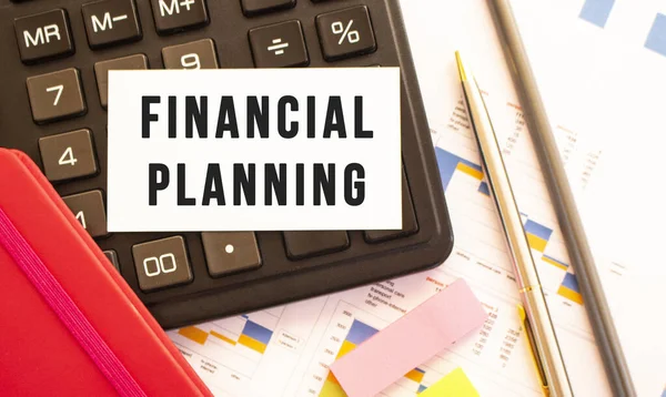 Text FINANCIAL PLANNING on white card with metal pen, calculator and financial charts. Business and financial concept