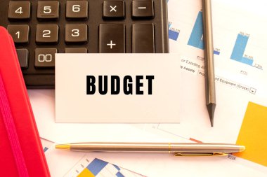 Metal kalem, hesap makinesi ve finansal tabloları olan beyaz kart üzerine metin bütçesi. İş ve mali konsept