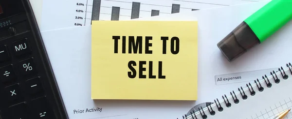 Ofis masasındaki mali tabloların üzerinde duran bir not defterinin sayfasına satma zamanı. Hesap makinesinin yanında. İş konsepti.