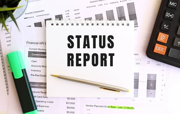 Beyaz arka planda, işaretleyicinin, hesap makinesinin ve ofis malzemelerinin yanında STATUS 'un yazılı olduğu not defteri. İş konsepti.