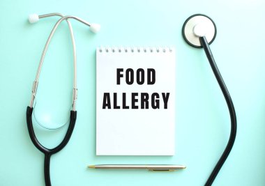 Mavi arka planda, steteskop ve üzerinde FOOD ALLERGY yazan beyaz bir not defteri var. Tıbbi konsept