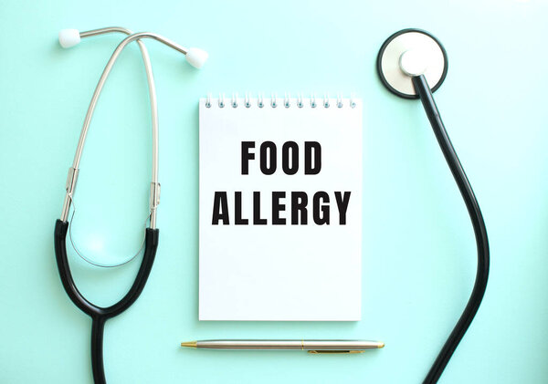 On a blue background, a stethoscope and a white notepad with the words FOOD ALLERGY. Medical concept
