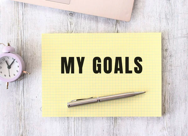 stock image The words MY GOALS written in a notebook lying on a wooden work table next to a laptop. Business concept.