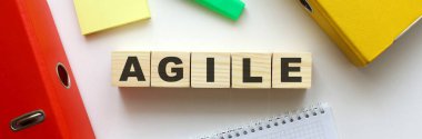 Ofis masasında AGILE sözcüğü olan tahta küpler. Dizin ve diğer ofis malzemeleri.