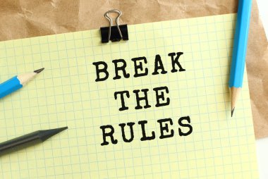 Buruşuk kraft kağıdının üzerindeki sarı bir kağıt parçasına yazılan kuralları kırın. Kalem ve ataç. İş konsepti.