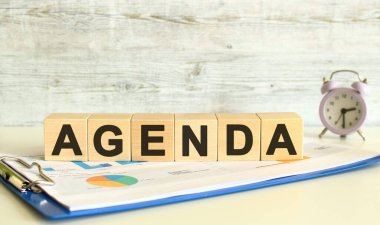 Tahta küpler, gri arka planda mali tabloların olduğu bir klasörde yatıyor. Küpler AGENDA kelimesini oluşturuyor. İş konsepti.