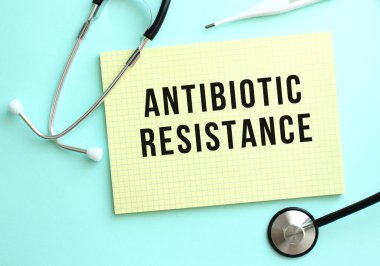 ANTIBIOTİK RESİSTANS, mavi arkaplanda steteskopun yanında duran sarı bir not defterine yazılmıştır. Tıbbi konsept