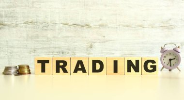 There are seven wooden cubes with letters on the table next to the coins. TRADING word. On a gray background. Front View Concepts
