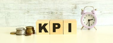 Bozuklukların yanındaki masada üç tahta küp ve harfler var. KPI kelimesi. Gri bir arkaplanda.