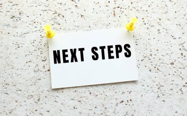 NEXT STEPS beyaz desenli bir duvara düğmeli bir karta yazılır. Ofis anımsatıcı.